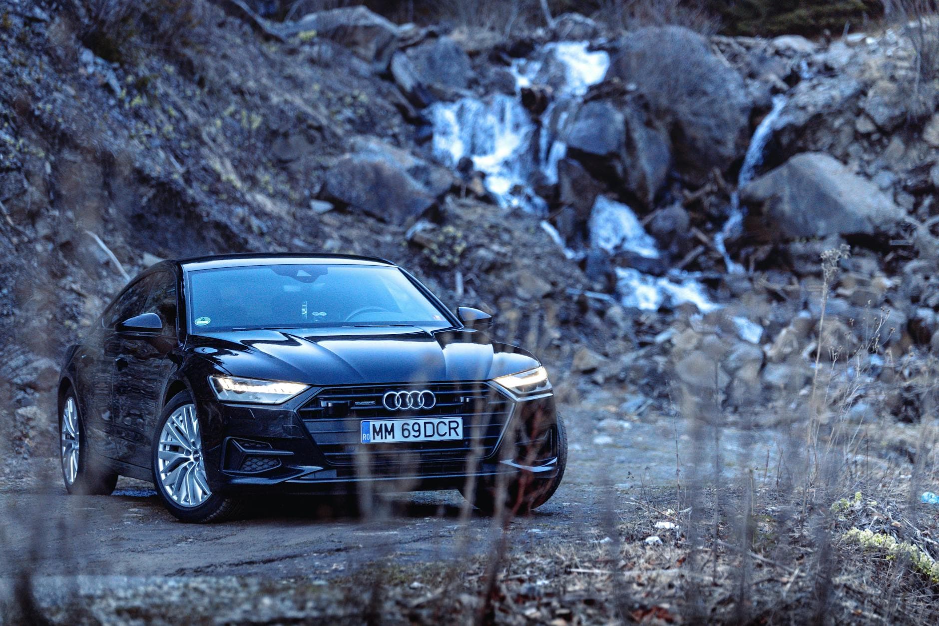 Schwarzer Audi auf Schotterweg vor felsigem Berghang mit mehreren Wasserläufen.
