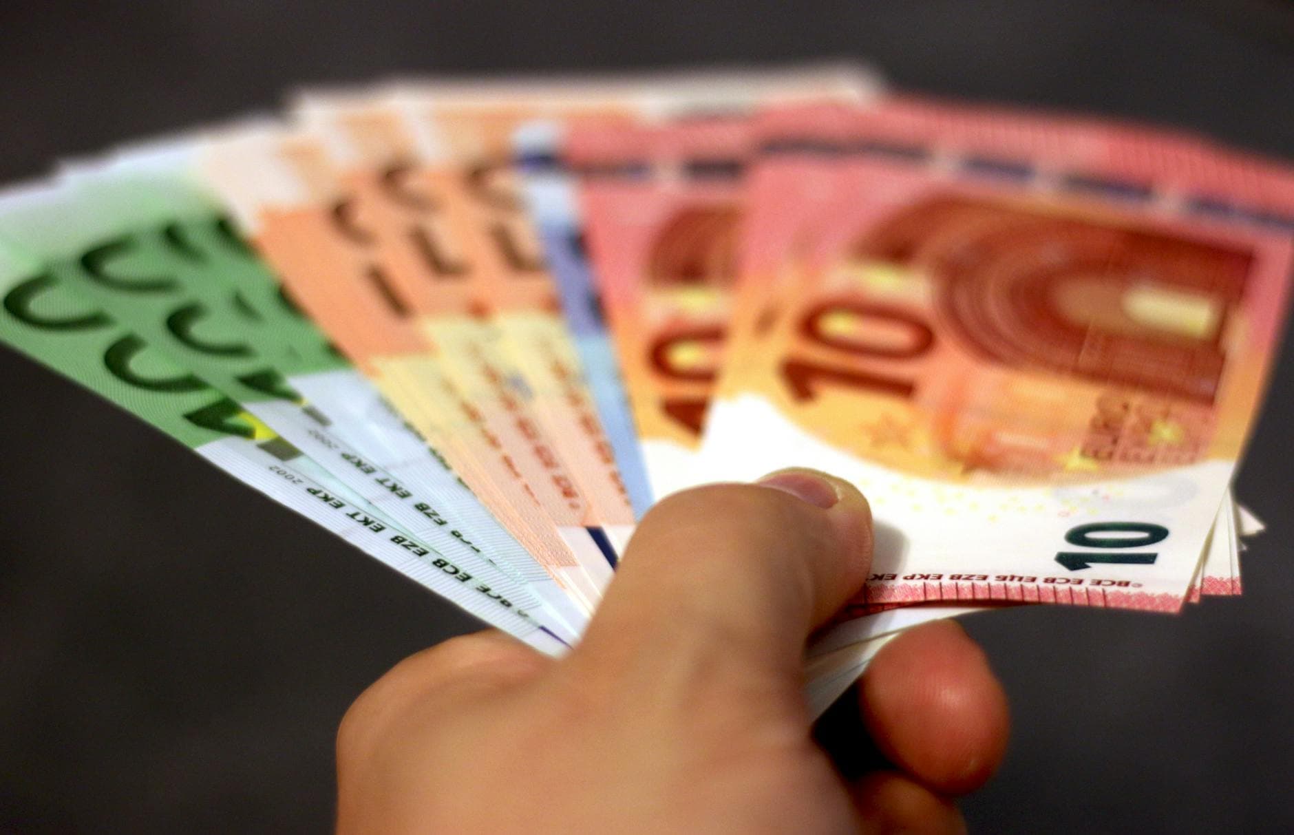 Eine Hand hält aufgefächerte Euro-Banknoten in den Werten 10, 20, 50 und 100 vor dunklem Hintergrund.
