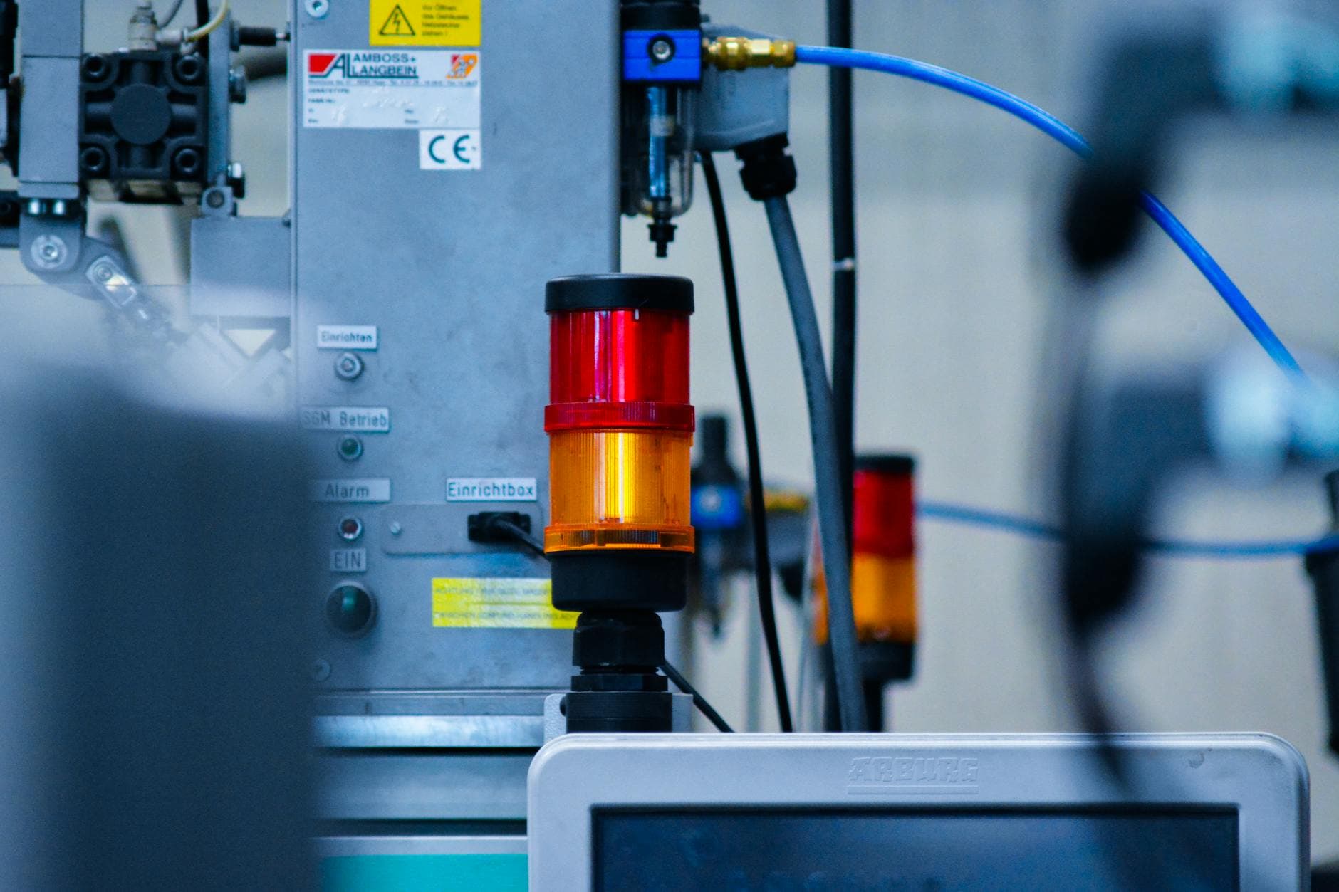 Detailansicht einer Industriemaschine mit leuchtender rot-oranger Signalsäule, blauen Pneumatikschläuchen und Monitor von ARBURG.