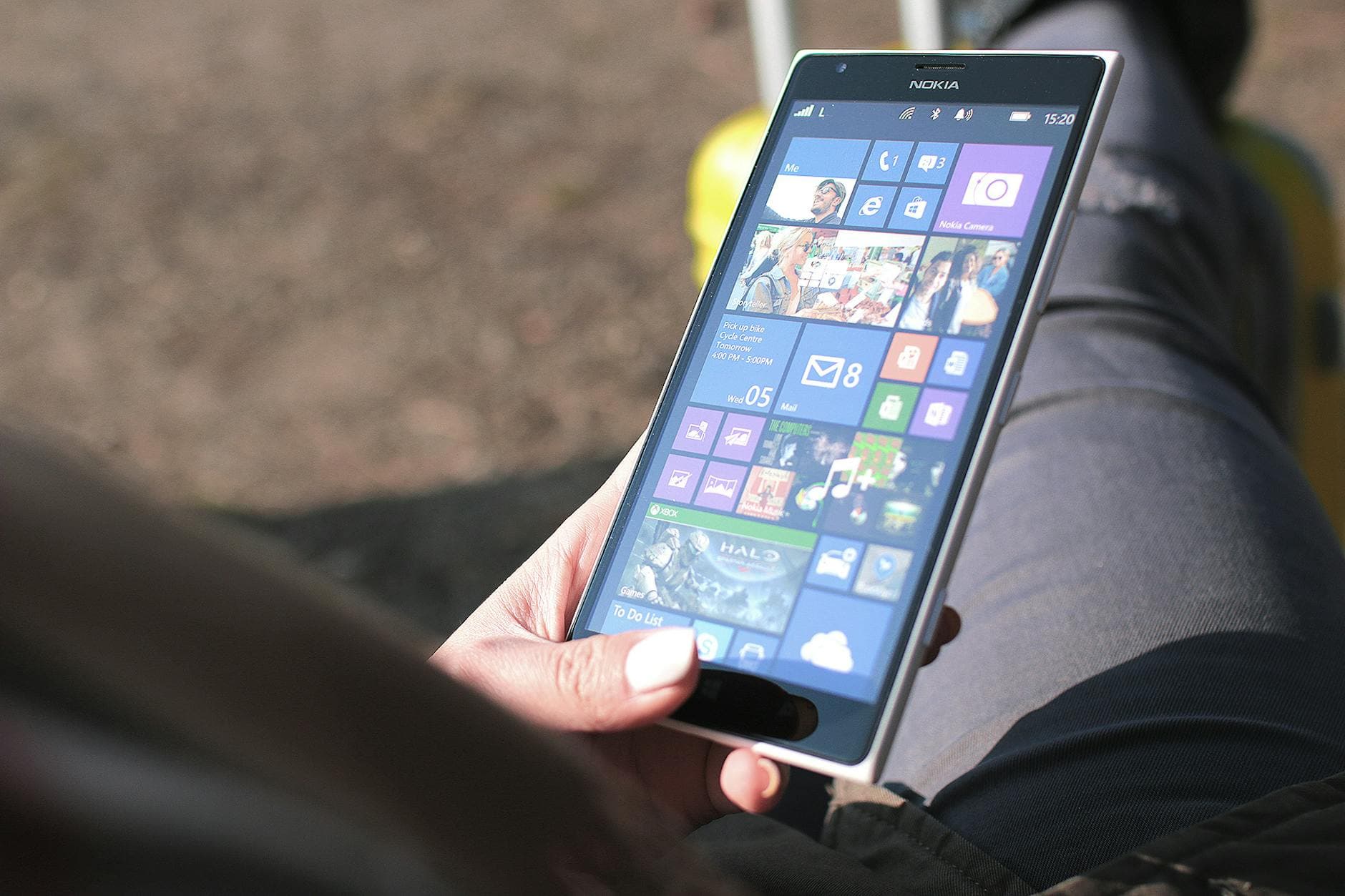 Eine Person hält ein weißes Nokia Smartphone mit Windows Phone Startbildschirm vor unscharfem Hintergrund.