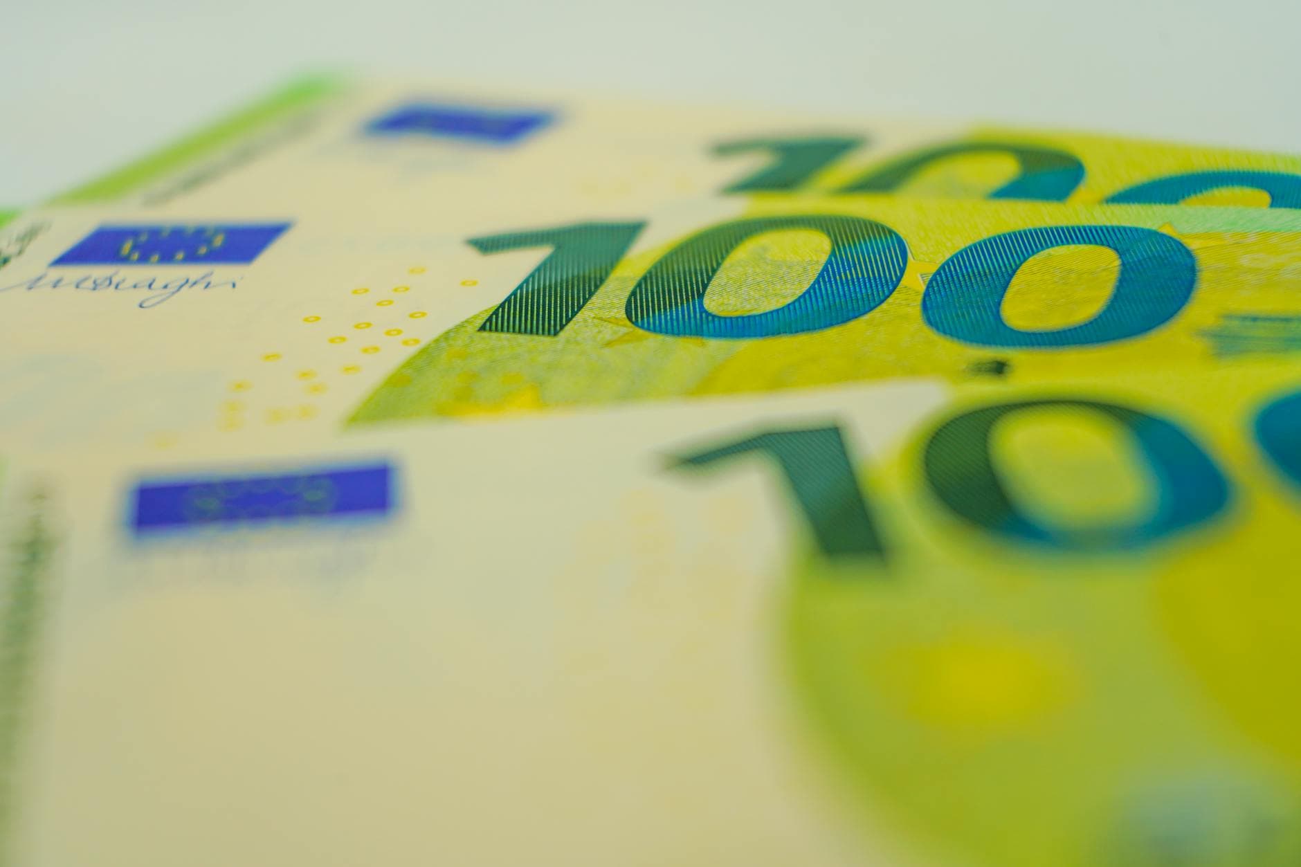Nahaufnahme mehrerer leicht überlappender 100-Euro-Banknoten mit sichtbaren "100"-Zahlen, EU-Flagge und Unterschrift.