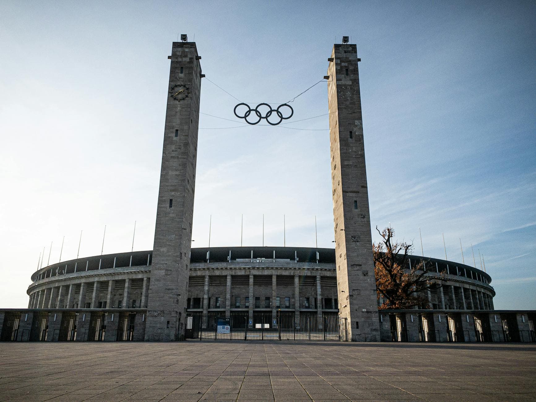 Eingang des Berliner Olympiastadions mit zwei Steintürmen, Uhr am linken Turm, Olympischen Ringen und gepflastertem Vorplatz.